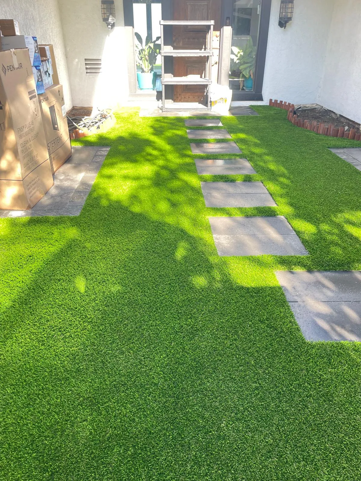 Artificial turf front entry with grey stone pavers leading to a wooden front door