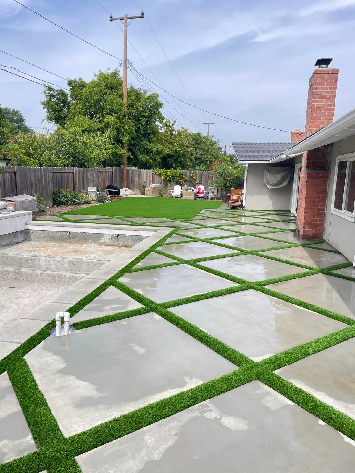 Large concrete pavers separated by strips of artificial turf across a backyard patio